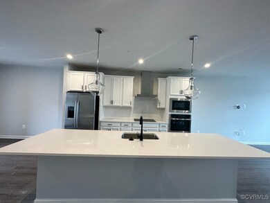 Kitchen with appliances with stainless steel finishes, a sink, wall chimney exhaust hood, baseboards, and a large island with sink