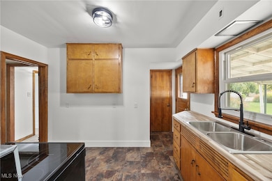 Kitchen featuring stone finish floors, brown cabinets, black range with electric stovetop, and light countertops