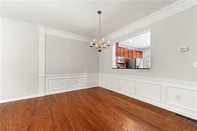 Dining area with a chandelier, dark wood finished floors, a wainscoted wall, ornamental molding, and a decorative wall