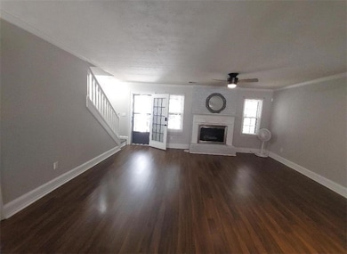 room with stairs, a fireplace with raised hearth, ornamental molding, a ceiling fan, and dark wood-style flooring