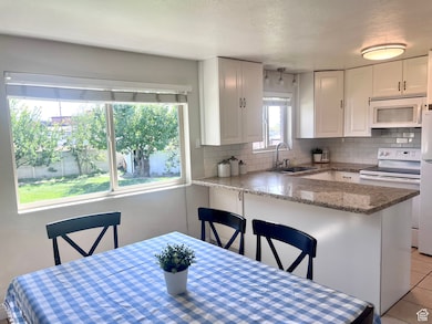Kitchen with white cabinetry, backsplash, white appliances, a kitchen breakfast bar, and a textured ceiling