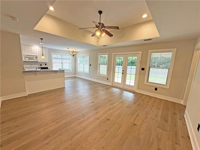 Unfurnished living room featuring a tray ceiling, light wood-style flooring, ceiling fan, recessed lighting, and a chandelier