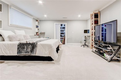 Carpeted downstairs bedroom featuring ornamental molding