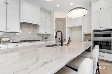 Kitchen featuring light stone counters, white cabinetry, hanging light fixtures, decorative backsplash, and recessed lighting