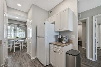 Kitchen with dark wood-type flooring, white cabinetry, dark stone counters, freestanding refrigerator, and recessed lighting
