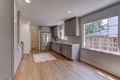 Kitchen featuring high end appliances, gray cabinetry, light countertops, backsplash, and light wood finished floors