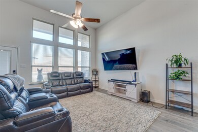 Living area with light wood finished floors, ceiling fan, and a high ceiling