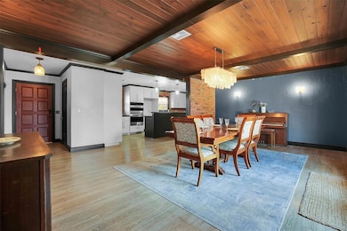 Dining space with a chandelier, light wood-style flooring, a textured wall, and a wood ceiling with exposed beams
