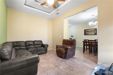 Living room featuring a tray ceiling, a chandelier, light tile patterned floors, and a ceiling fan