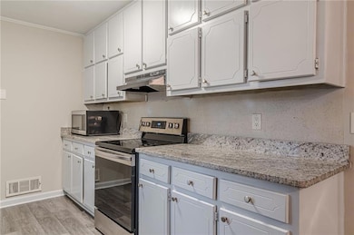 Kitchen with stainless steel appliances, under cabinet range hood, crown molding, white cabinets, and light wood finished floors