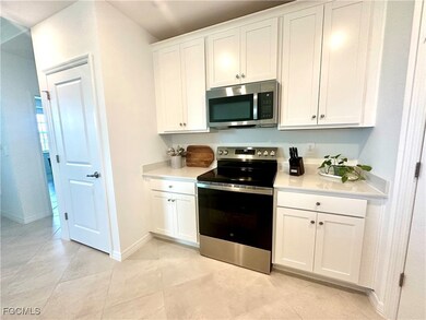 Kitchen with stainless steel appliances, white cabinets, light tile patterned flooring, and light stone counters