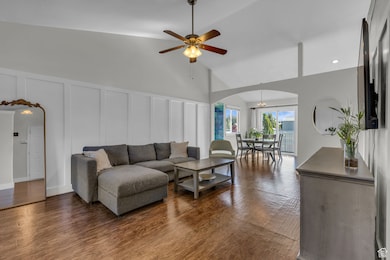 Living room featuring a decorative wall, dark wood finished floors, arched walkways, ceiling fan, and high vaulted ceiling