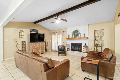 Tiled living room with vaulted ceiling with beams, ceiling fan, and a brick fireplace