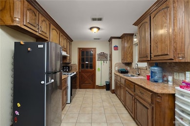 Kitchen with freestanding refrigerator, tasteful backsplash, black range with gas stovetop, and light tile patterned floors