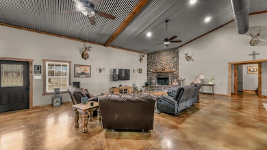 Living area featuring finished concrete floors, high vaulted ceiling, a stone fireplace, and beamed ceiling