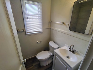 Half bathroom featuring baseboards, toilet, wood f