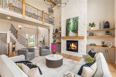 Living area with wood finished floors, stairs, a stone fireplace, a high ceiling, and a chandelier