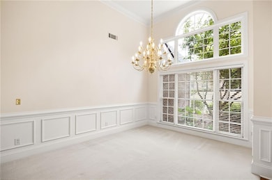 Empty room with a chandelier, ornamental molding, light colored carpet, a wainscoted wall, and a decorative wall