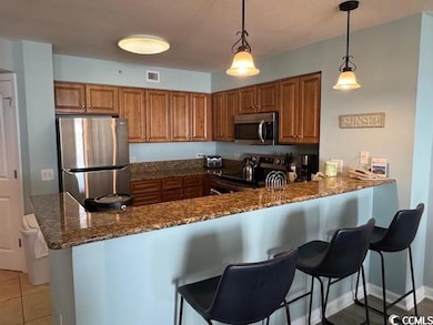 Kitchen with brown cabinetry, decorative light fixtures, appliances with stainless steel finishes, and a breakfast bar