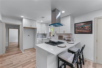 Kitchen featuring island range hood, a sink, a peninsula, light countertops, and light wood-style flooring