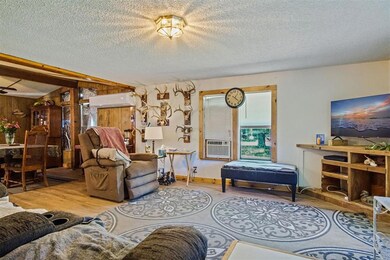 Living room with wood finished floors, a wall unit AC, a textured ceiling, wood walls, and baseboards