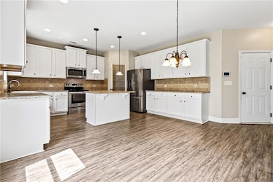 Kitchen with appliances with stainless steel finishes, wood finished floors, white cabinetry, decorative backsplash, and recessed lighting