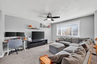 Living room with carpet flooring, a ceiling fan, a desk, and a textured ceiling