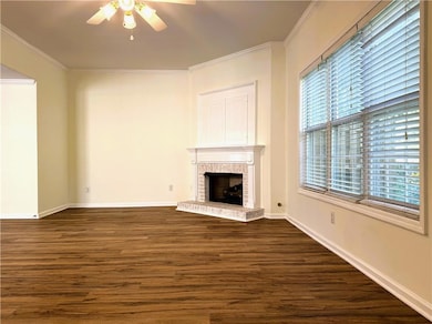 Unfurnished living room featuring dark wood-type flooring, crown molding, a brick fireplace, and ceiling fan