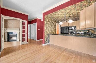 Kitchen featuring wallpapered walls, light wood finished floors, a premium fireplace, black appliances, and light brown cabinetry
