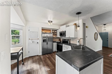 Kitchen featuring stainless steel appliances, dark countertops, open shelves, a peninsula, and a textured ceiling