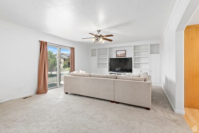 Living area with a ceiling fan, crown molding, a textured ceiling, carpet flooring, and built in features