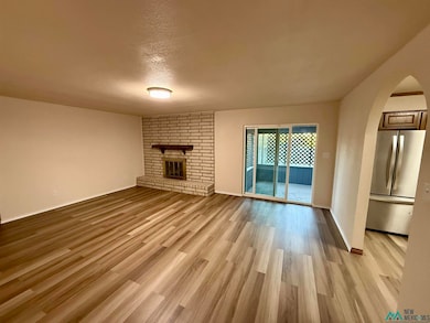 Unfurnished living room featuring a textured ceiling, light wood finished floors, arched walkways, and a brick fireplace