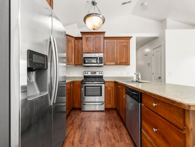 Kitchen with appliances with stainless steel finishes, brown cabinetry, dark wood-style floors, light countertops, and decorative light fixtures