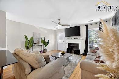 Living room with light wood-style floors, a fireplace with flush hearth, plenty of natural light, and a ceiling fan