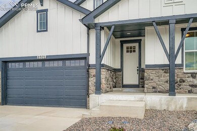 View of exterior entry with board and batten siding, a garage, a porch, driveway, and stone siding