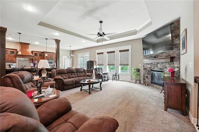 Living area featuring a raised ceiling, light colored carpet, a fireplace, ceiling fan, and recessed lighting