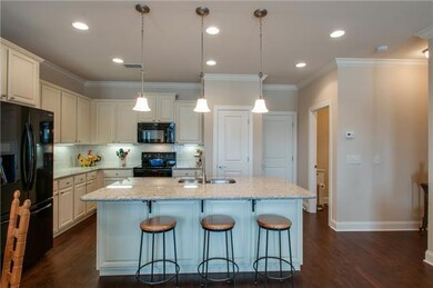 A large island with seating for three and pendant lighting is the centerpiece of the kitchen and open den living space.