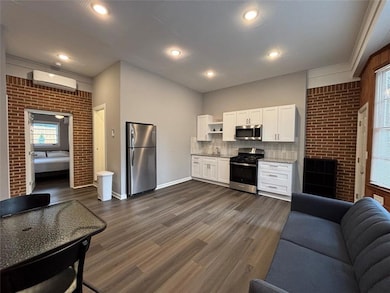 Open-concept kitchen and living area featuring appliances with stainless steel finishes, open floor plan, a wall unit AC, white cabinetry, and dark wood-style flooring