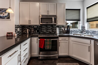 Kitchen featuring appliances with stainless steel finishes, backsplash, pendant lighting, dark stone counters, and dark wood-type flooring