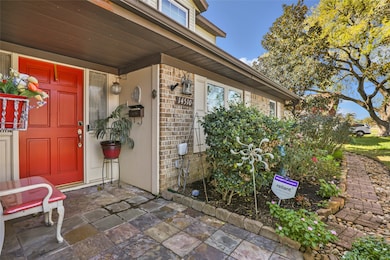 Charming home entrance with a vibrant red front door, sheltered by an overhang. The area features a mix of brick and siding, a well-maintained garden with decorative plants, and a stone pathway, creating a welcoming curb appeal.