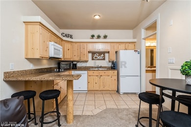 Kitchen with light brown cabinets, a kitchen breakfast bar, a sink, white appliances, and light tile patterned floors