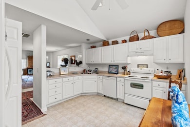 Kitchen featuring white appliances, white cabinets, light countertops, under cabinet range hood, and vaulted ceiling