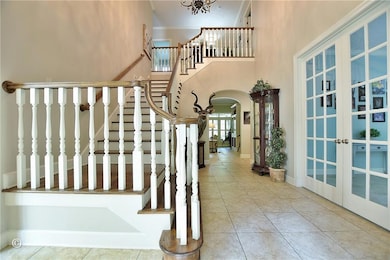 Stairs featuring arched walkways, tile patterned flooring, a towering ceiling, french doors, and a chandelier