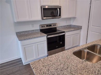Kitchen featuring stainless steel appliances, white cabinets, light stone countertops, and dark wood finished floors
