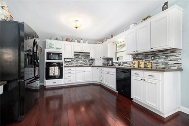Kitchen featuring black appliances, decorative backsplash, dark wood-type flooring, white cabinetry, and dark countertops