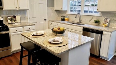 Kitchen with stainless steel appliances, white cabinetry, light stone countertops, dark wood-style floors, and tasteful backsplash