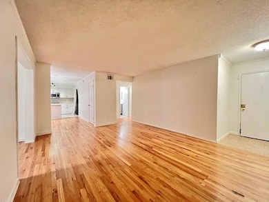 Unfurnished living room featuring a textured ceiling, light wood-type flooring, and crown molding