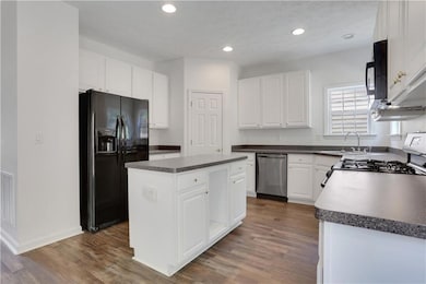 Kitchen featuring black appliances, a sink, dark countertops, a center island, and dark wood-type flooring