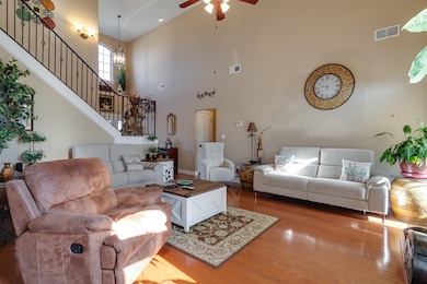 Living room with wood finished floors, a ceiling fan, stairway, and a high ceiling