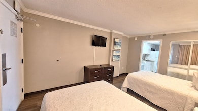 Bedroom with dark wood-style floors, a textured ceiling, crown molding, and ensuite bathroom
